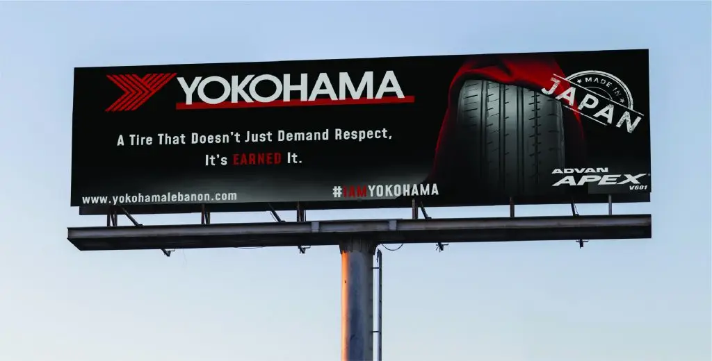 Billboard advertisement for Yokohama tires, featuring the Yokohama logo on the left with the text 'A Tire That Doesn’t Just Demand Respect, It’s Earned It.' Below the text is an image of a tire partially covered by a red cloth. A circular stamp-like design near the tire reads 'JAPAN.' At the bottom, the website 'www.yokohamatire.com' and the Yokohama logo are displayed along with the text 'ADVAN APEX V601.'